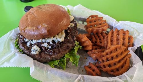 A juicy burger topped with blue cheese and lettuce, served with crispy waffle fries on a green table.
