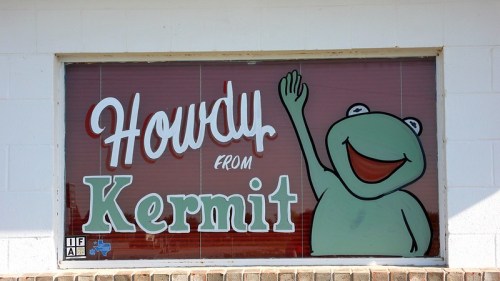 A sign reading "Howdy from Kermit" featuring a smiling green frog waving.