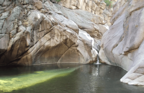 A serene natural pool surrounded by smooth, rocky cliffs and sunlight reflecting on the water's surface.