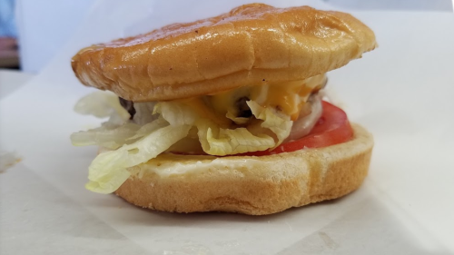 A close-up of a hamburger with a toasted bun, lettuce, tomato, cheese, and a patty, resting on a white surface.