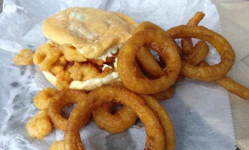 A sandwich with fried chicken and mayonnaise, accompanied by crispy onion rings on a paper wrapper.