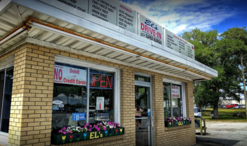 A brick drive-in restaurant with a sign reading "Eli's," featuring open windows and a flower box outside.