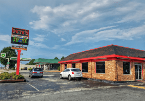 A brick building with a red roof, featuring a sign for "Pete's Burgers & More," with a drive-thru and nearby gas station.