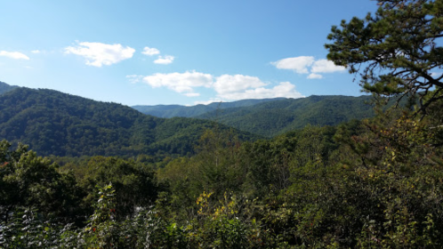 A scenic view of lush green mountains under a clear blue sky with scattered clouds.