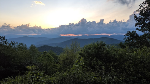 Sunset over rolling mountains, with a colorful sky and lush greenery in the foreground.
