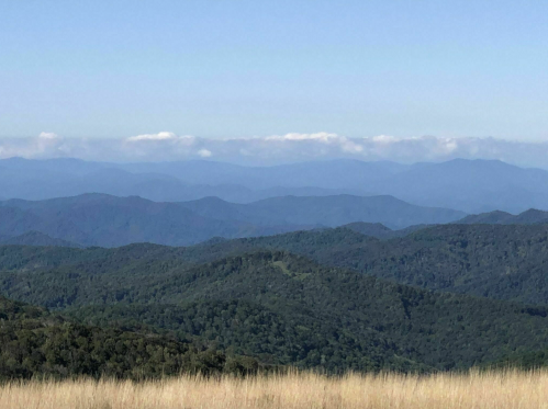 A panoramic view of rolling green mountains under a clear blue sky with distant clouds.