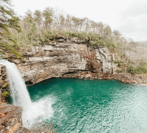 A waterfall cascades into a turquoise pool surrounded by rocky cliffs and trees.