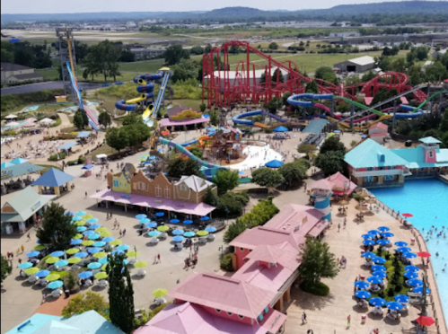 Aerial view of a vibrant water park with slides, pools, and colorful umbrellas, bustling with visitors on a sunny day.