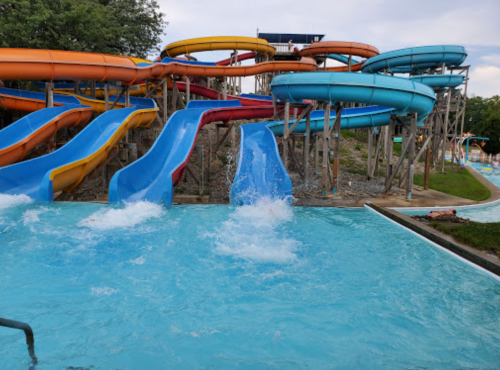 Colorful water slides at a water park, with splashes in the pool below and a cloudy sky above.