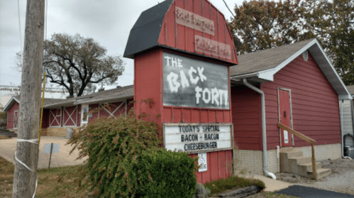 A red building with a sign reading "The Back Fort" and a special for bacon cheeseburgers. Trees in the background.