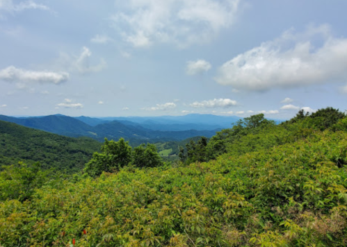 A panoramic view of rolling green hills and mountains under a partly cloudy sky.