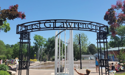 Archway reading "Ernest G. Lawrence Park" with a fountain and trees in a sunny park setting. Children play nearby.