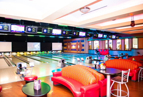 A vibrant bowling alley featuring colorful seating, multiple lanes, and screens displaying scores and announcements.