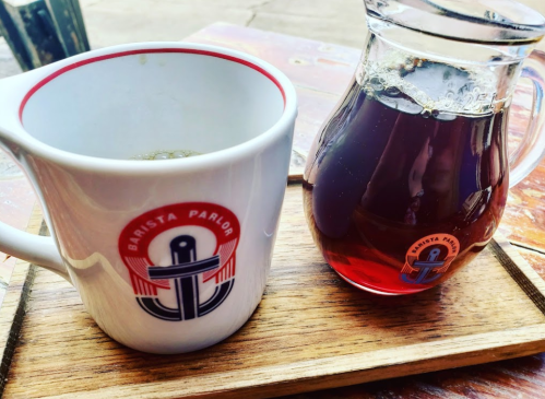 A white mug with a logo and a glass carafe of coffee on a wooden tray.
