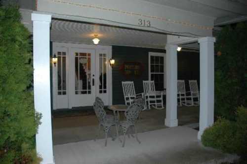 A cozy porch with white rocking chairs and a small table, illuminated by soft lighting at night.