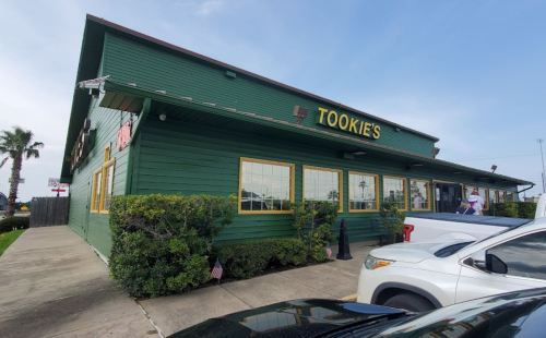 Exterior of Tookie's restaurant, a green wooden building with large windows and palm trees nearby.