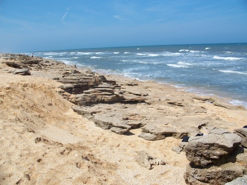 Rocky beach with golden sand and gentle waves under a clear blue sky.