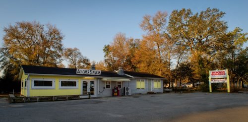 A small burger restaurant with a yellow exterior, surrounded by trees, under a clear sky during sunset.