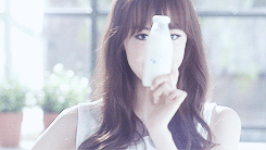 A person holds a small milk bottle in front of their face, smiling playfully in a bright, indoor setting.