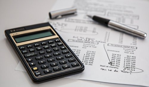A calculator, pen, and financial documents with calculations and notes on a desk.