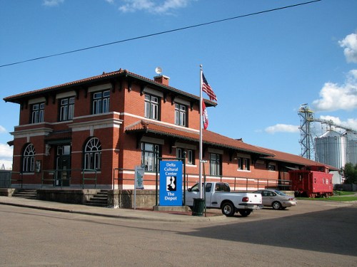 Historic brick building with a sign for the Delta Cultural Center, featuring an American flag and nearby vehicles.
