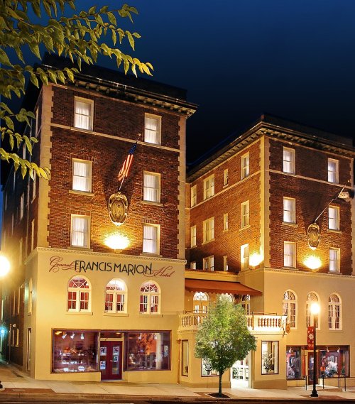Historic Francis Marion Hotel at night, featuring brick architecture, illuminated windows, and a welcoming entrance.