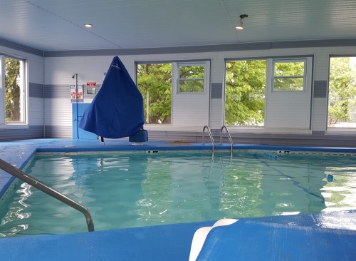 Indoor swimming pool with clear water, a blue cover draped over a section, and large windows letting in natural light.