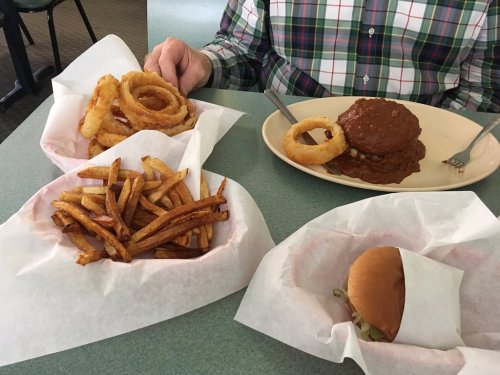 A table with a plate of onion rings, a burger, fries, and a plate of meatloaf with gravy.