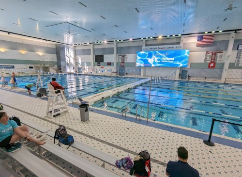 A spacious indoor swimming pool with lanes, bleachers, and a large digital screen displaying "Hattiesburg."