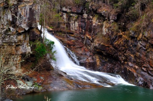 A serene waterfall cascades over rocky cliffs into a tranquil pool, surrounded by lush greenery and rugged terrain.