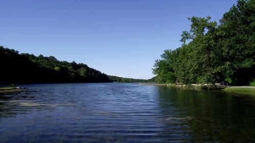 A serene lake surrounded by lush greenery under a clear blue sky.