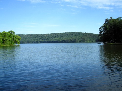 A serene lake surrounded by lush green trees and rolling hills under a clear blue sky.