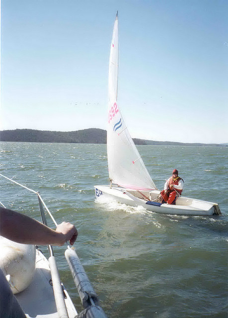 A person sailing a small boat on a lake, with a clear blue sky and hills in the background.