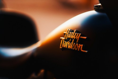 Close-up of a Harley-Davidson logo on a motorcycle, featuring a sleek black surface and warm lighting.