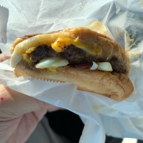 A close-up of a cheeseburger with melted cheese, bacon, and a soft bun, held in a hand.