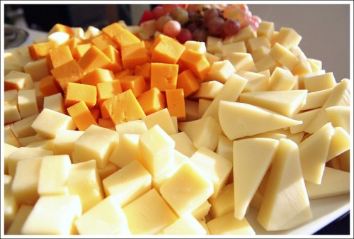 A platter of assorted cheese cubes, including yellow cheddar and white varieties, with a few grapes in the background.