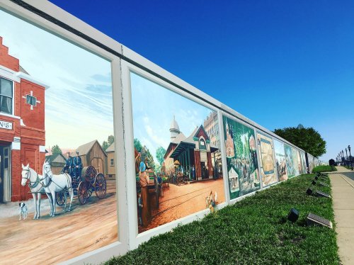 A colorful mural depicting historical scenes with horses, buildings, and people against a clear blue sky.