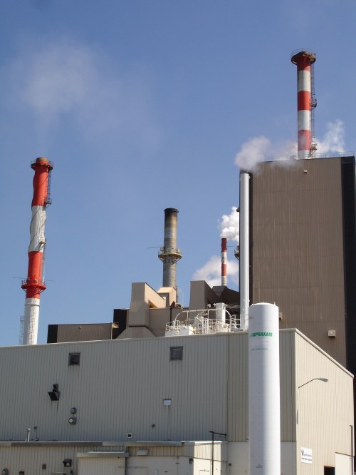 Industrial facility with tall smokestacks emitting steam against a clear blue sky.