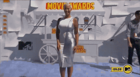 A woman in a white dress poses on a blue carpet at an awards event, with a backdrop featuring "MTV Movie Awards."