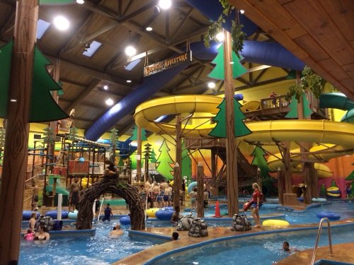 Indoor water park featuring colorful slides, a play area, and a pool filled with people enjoying the attractions.