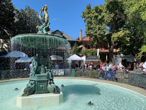 A decorative fountain with water cascading, surrounded by trees and people at an outdoor event.