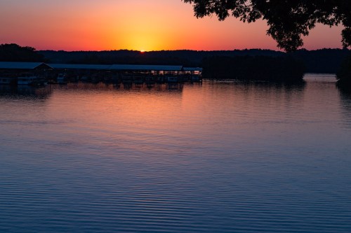 A serene sunset over a calm lake, with vibrant orange and purple hues reflecting on the water's surface.