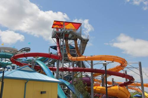 A colorful water slide tower with multiple twisting slides under a blue sky and fluffy clouds.