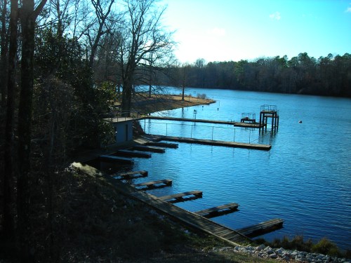 A serene lake scene with wooden docks, trees lining the shore, and a clear blue sky reflecting on the water.