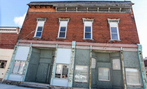 Abandoned brick building with ornate details, featuring large windows and peeling paint on the lower facade.