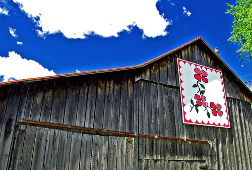 A rustic barn with a colorful flower mural against a bright blue sky and fluffy white clouds.