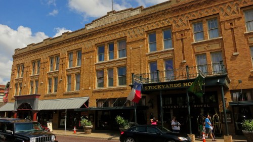 Historic brick building with decorative architecture, featuring the Stockyards Hotel and Texas flags. Sunny day.