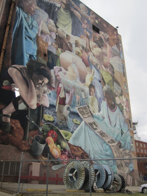 A large mural depicting diverse people engaged in various activities, surrounded by vibrant colors and imagery of food and community.