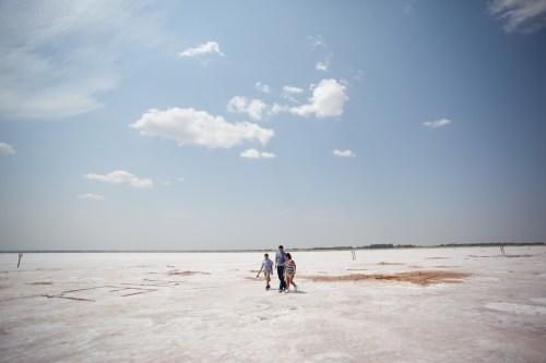 A family walks across a vast, white salt flat under a blue sky with scattered clouds.