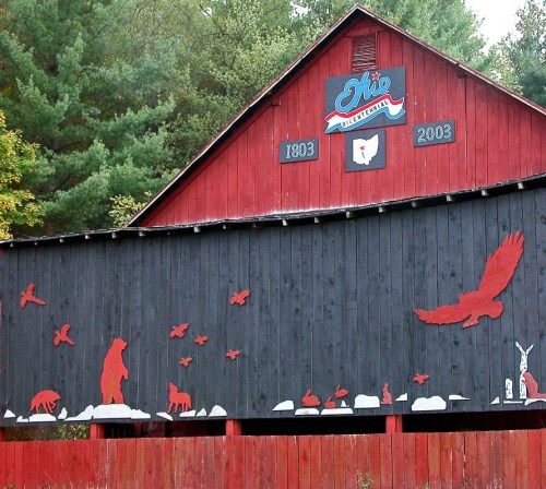 A red and black barn with wildlife silhouettes, featuring a bear, birds, and a rabbit, set against a forest backdrop.